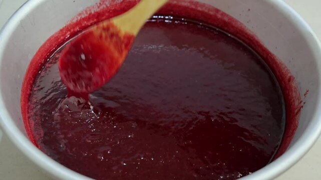 a man cooks plum jam in an aluminum basin, stirring the jam with a wooden spoon