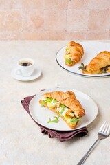 Breakfast, sandwich croissant with fried chicken, arugula and fresh pineapple on a light plate on a light concrete background.