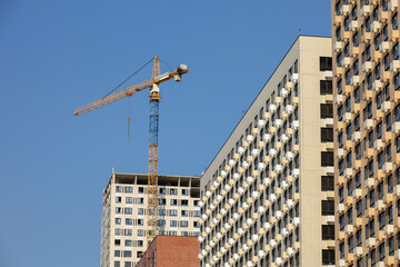 Tower crane and unfinished buildings on background of blue sky. Housing construction, apartment blocks in city