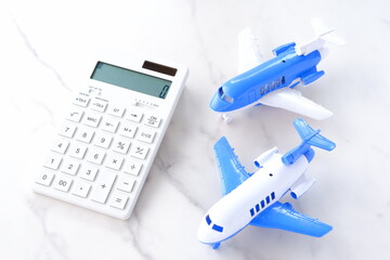 電卓と飛行機で、高騰する航空券代と、高騰する旅行代金のイメージ
