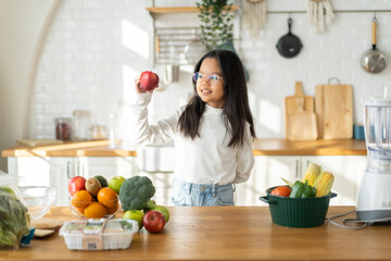 Asian girl holding red apple in the kitchen, healthy eating habits for children, nutrition education, fresh fruit choice, young kid learning about healthy food, happy child healthy lifestyle concept