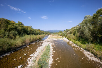 Beautiful mountain landscape on a sunny day. Natural coastline. A small amount of water in the river. Beskid Mountains. The Soła River. View from the 