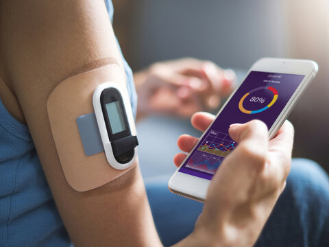 Close-up of a person using a health monitoring device on their arm and checking data on a smartphone app.