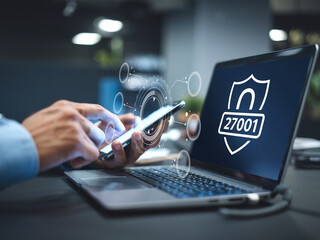 Person using a smartphone and laptop with cybersecurity ISO 27001 certification symbol, representing data protection and information security.