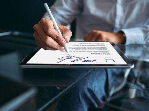 Person using a digital tablet to sign a document electronically. Modern technology for electronic signatures and paperless business processes.