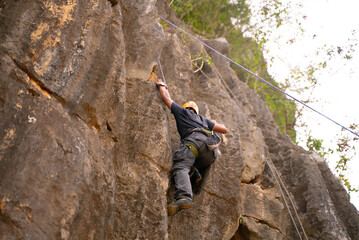 Rock Climber Mid-Ascent on Steep Cliff Surrounded by Lush Greenery
