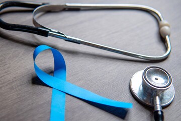 A blue ribbon and a stethoscope placed on a wooden surface. Male health, prostate cancer awareness...