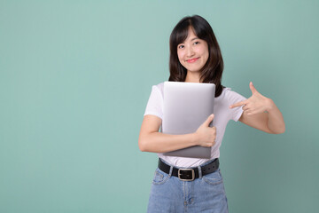 Technology lover concept. Cheerful asian woman pointing finger to laptop. Casual female geek hug a computer isolated on green background. Back to school concept for advertisement.