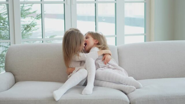 Happy family sisterly love. Two funny little twin sisters girls hugging with love care playing together at home indoors. Happy children lifestyle. Identical twin girls hugs. Girls friendship and youth