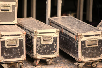 A row of old, dirty concert boxes with wheels on the bottom.