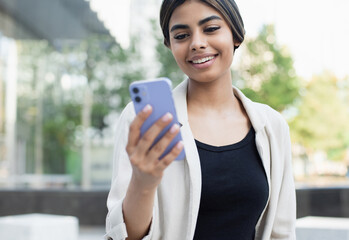 Young beautiful woman using smartphone in a city. Smiling student girl texting on mobile phone...
