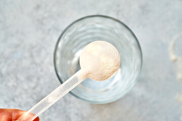 Collagen powder in a plastic measuring spoon above a glass cup of water, top view
