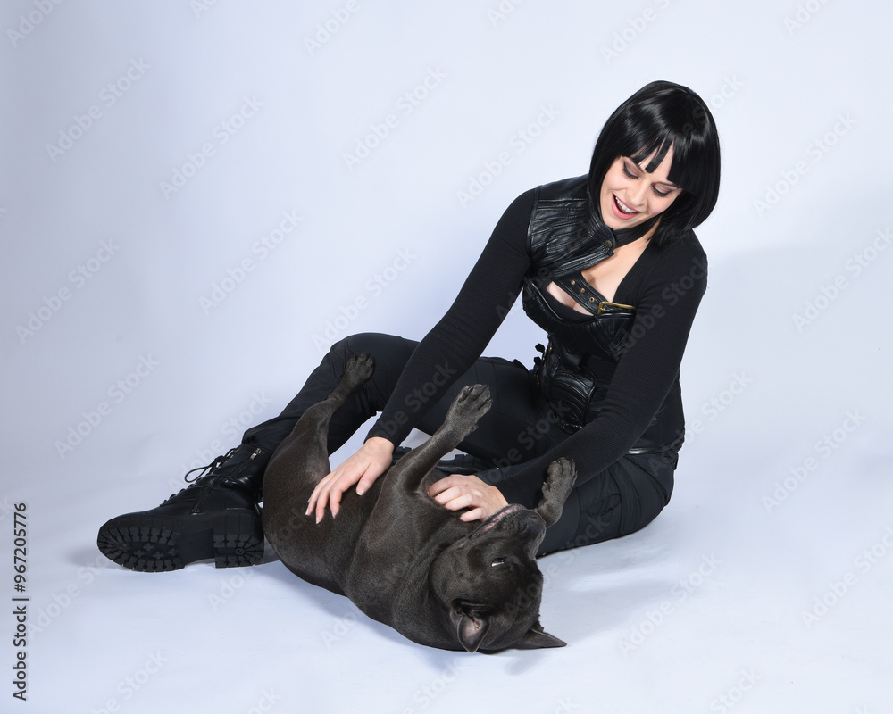 Canvas Prints Full length portrait of beautiful black female model wearing sci fi futuristic dystopian leather bodysuit costume, with animal dog pet companion. sitting pose, isolated white studio background.