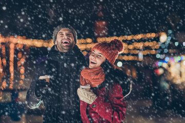 Photo of two people with hot beverage in hands spending x-mas evening together telling humorous jokes having best time wearing warm jackets