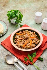Stew, beef stew with beans and carrots in a ceramic plate on a green concrete background. Beef recipes.