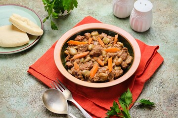 Stew, beef stew with beans and carrots in a ceramic plate on a green concrete background. Beef recipes.