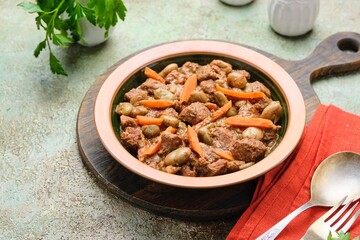 Stew, beef stew with beans and carrots in a ceramic plate on a green concrete background. Beef recipes.