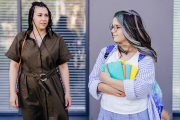 Mature mother sending teener daughter to school outdoor. Happy girl with colorful hairstyle holding...
