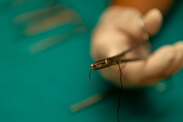 A surgeon's hand is holding a curved surgical needle using a needle holder Mayo-Hegar)