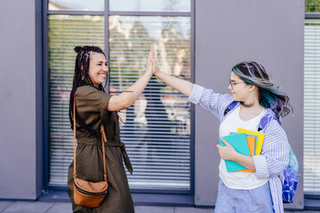Mother and daughter giving high five in front of school. Mother take her daughter to school. Little...