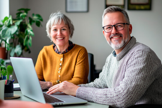 Smiling senior couple working on a laptop together in a cozy home office. Mature teamwork and collaboration concept. Design for home workspace, remote work, and partnership