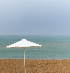 umbrella against the sun on a sandy beach on a gloomy rainy day. abstraction on the theme of the end of the beach tourist season