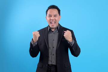 Excited Asian businessman with fists in the air celebrating victory isolated on blue background