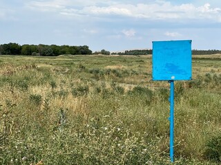 Empty sign in a field with green grass and trees