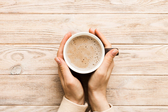 Minimalistic style woman hand holding a cup of coffee on Colored background. Flat lay, top view cappuccino cup. Empty place for text, copy space. Coffee addiction. Top view, flat lay