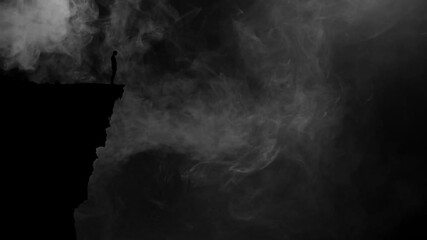 Dark Silhouette of a Person Standing on the Edge of a Cliff Backlit With Fog