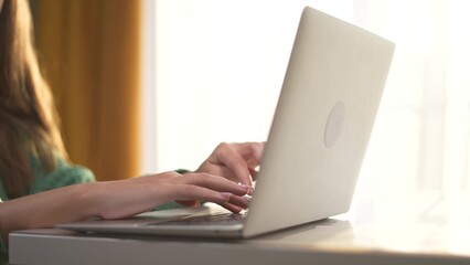 Naklejka premium Girl with her hands typing on laptop. woman work from home concept. hands of a woman typing on a lifestyle laptop. a girl with large hands typing on a laptop.