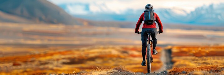 A mountain biker wearing a red jacket riding through a scenic open landscape, with distant mountains in the background, embracing adventure and nature.