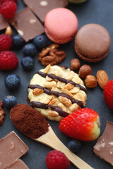 Macarons, chocolate, cookies, berries and various nuts on dark blue background. Selective focus.