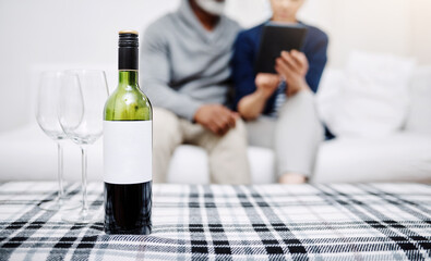 Wine, mockup space and glasses on table in home for marriage anniversary date night together. Romance, bonding and couple relax on sofa with bottle of alcohol beverage for love celebration at house.