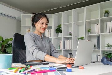 Graphic designer typing on laptop surrounded by design tools