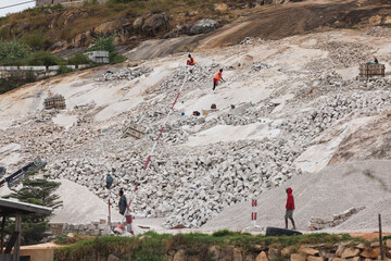 Workers extracting stone in suburban Antananarivo, Madagascar, on a rugged mining site surrounded...