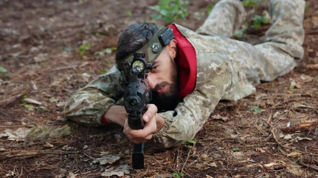 Camouflage gear, Tactical training, Marksman training. In forested training setting, Laser tag sharpshooter lies flat in camo gear, carefully targeting with paintball gun that has precision sight.