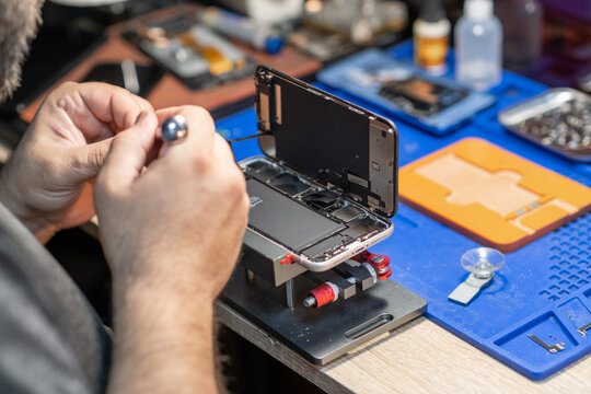 A skilled technician performs phone repair and replaces a battery in a well-organized workshop with tools and parts readily available