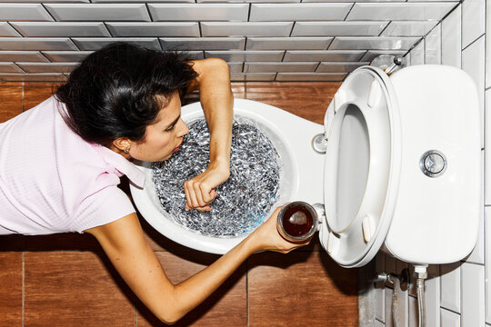 Woman leans over toilet filled with shiny foil, holding glass of drink in her hand, suggesting party or late-night scene. Concept of holidays, celebration, festive mood. Pop art style.