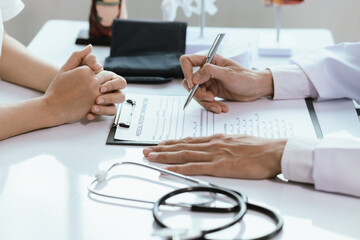 Asian male doctor consults with patient in clinic, reviews medical documents and uses stethoscope to diagnose health conditions, and confidently provides professional advice and care.