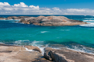 Western Australia, Green's Pool in Denmark, rocky coastline with clear water and distant waves under a partly cloudy sky.