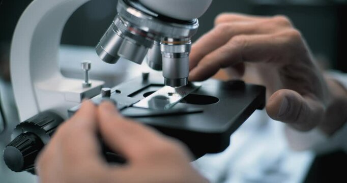 Close up of microbiologist or chemist putting fossil specimen under microscope for analysis. Scientist or archaeologist works with professional equipment in advanced archaeological science laboratory.