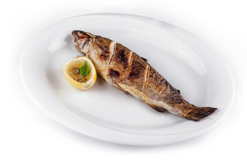 Grilled trout lying on white plate with lemon and capers