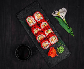 California uramaki sushi rolls with salmon and avocado decorated with red tobiko caviar on black slate plate