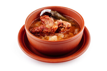 Steaming hot soup with meat and potatoes served in a clay pot on a plate