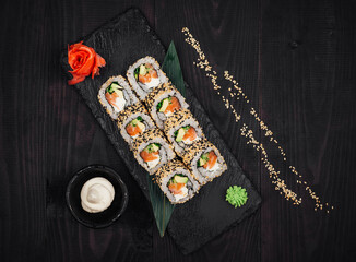 Sushi rolls set served on black stone plate on dark wooden table