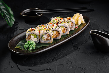 Sushi rolls covered with sesame seeds lying on a black plate on dark stone table