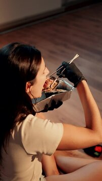 Young woman eating sushi burger with chopsticks while sitting in lotus position. Japanese food concept. Sushi burger in hands.Vertical vedeo 4K