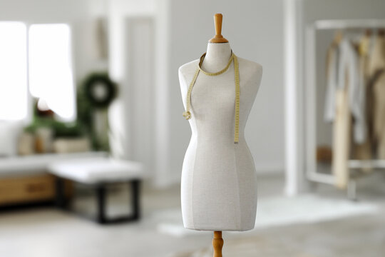 Elegant tailor's mannequin displayed with a measuring tape draped around it in a minimalistic and brightly lit modern design studio setup, emphasizing creativity and craftsmanship.