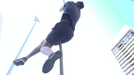 A teenager plays sports on an outdoor sports ground by climbing up a rope